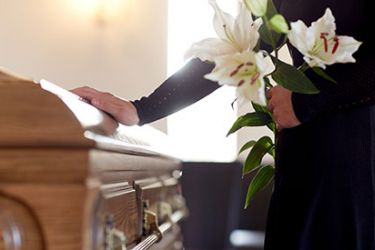 Photographie d'une personne tenant des fleurs et la main sur le cercueil